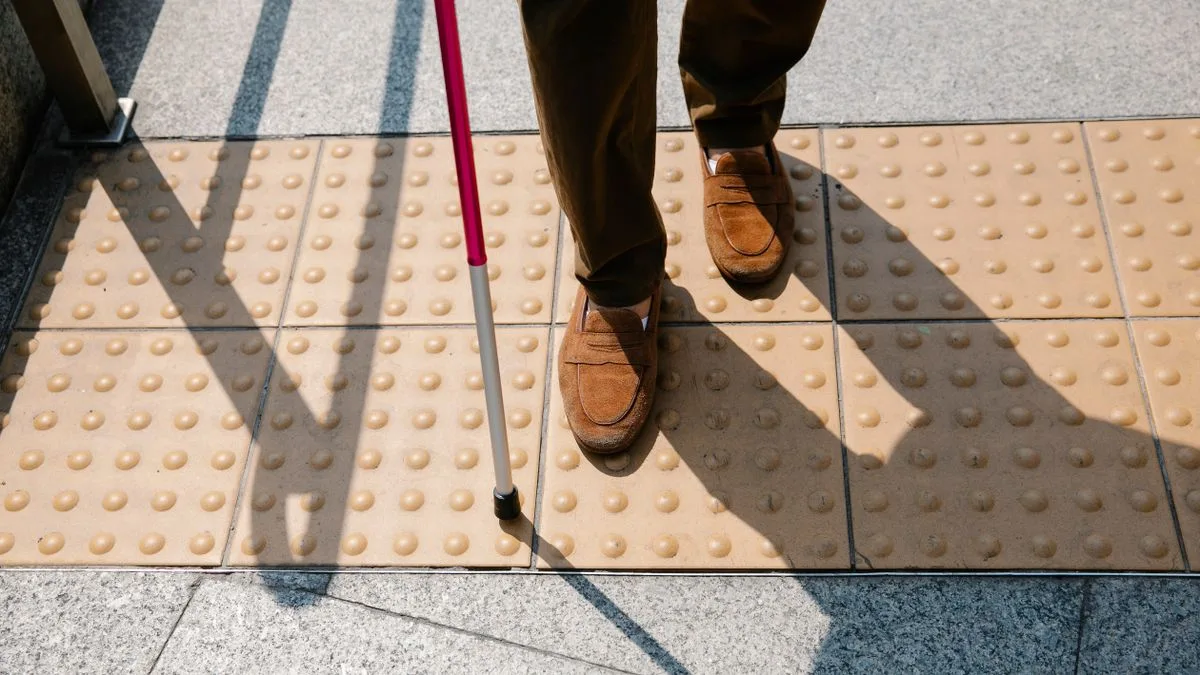 Close-up of a blind person walking on tactile paving with a cane, emphasizing accessibility.