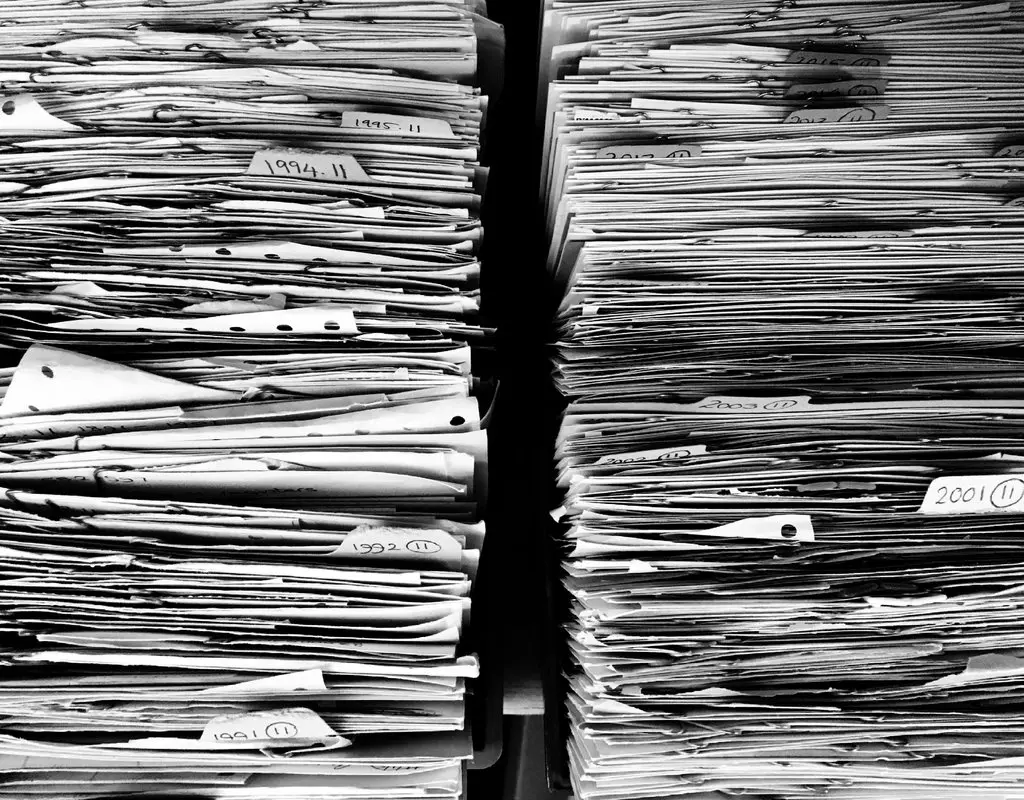 Two tall stacks of paper files and documents with handwritten year labels ranging from 1991 to 2015