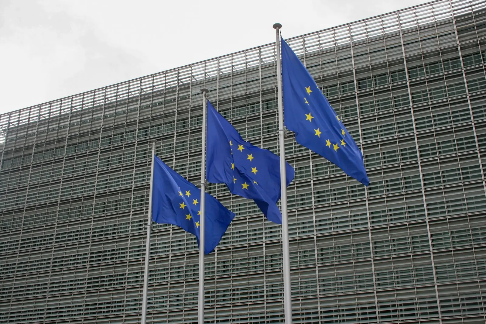 Three European Union flags flying in front of a building in Brussels